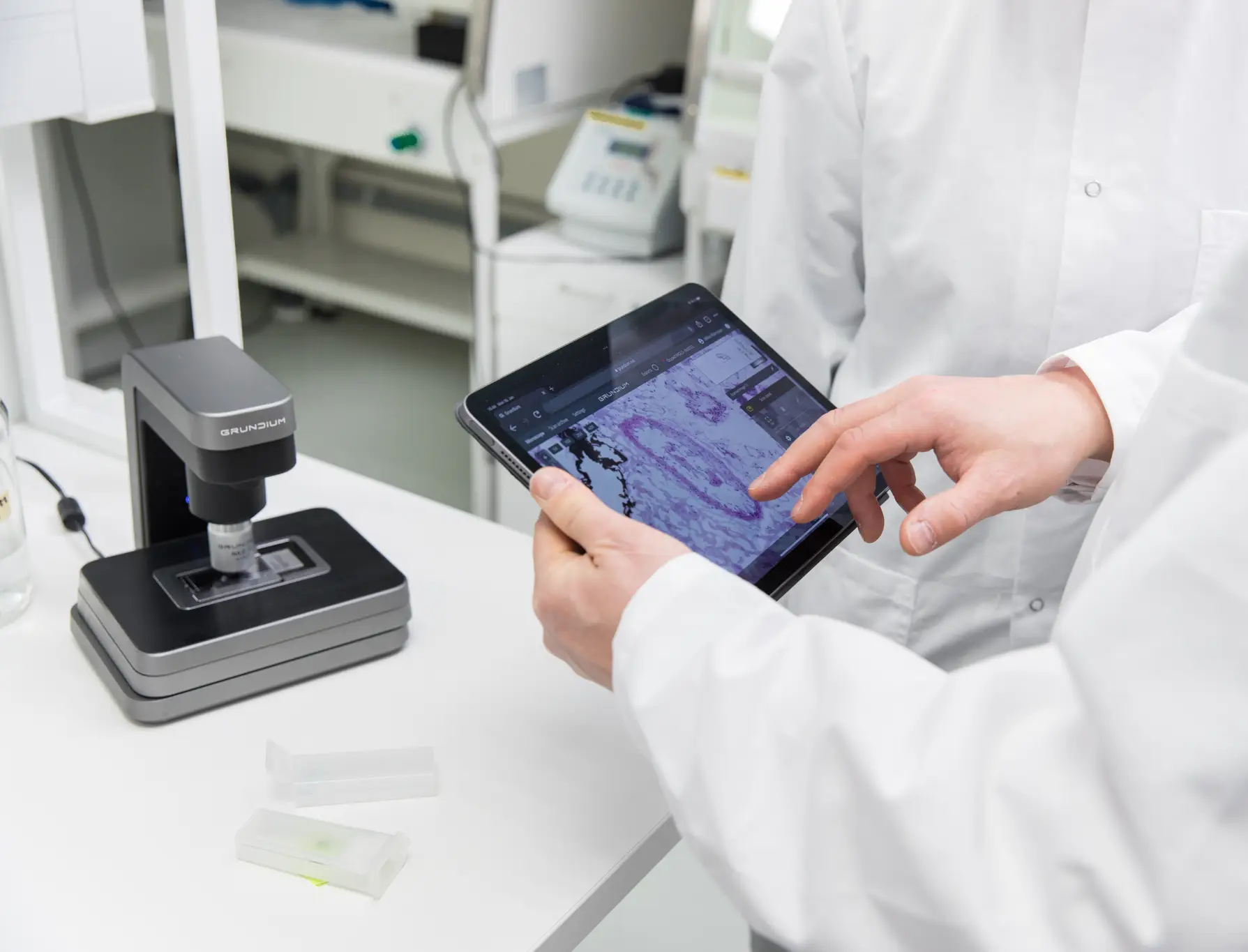 A pathologist in laboratory environment using an iPad to review a sample scanned with the Ocus scanner on the desk